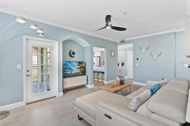 living room featuring ceiling fan, ornamental molding, a textured ceiling, and light wood-type flooring