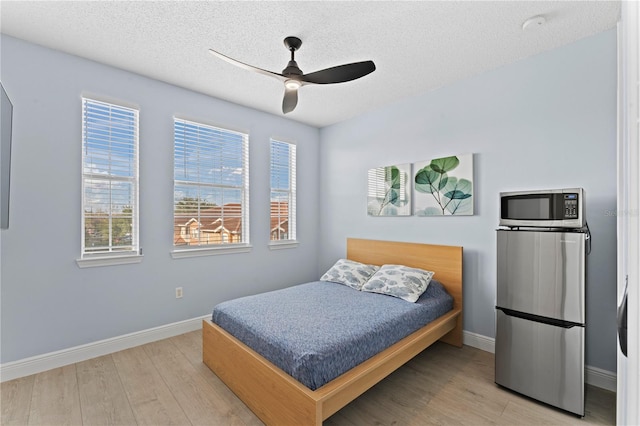 bedroom featuring ceiling fan, stainless steel fridge, light hardwood / wood-style flooring, and a textured ceiling