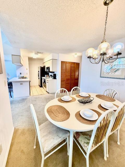 dining area featuring a chandelier, light colored carpet, and a textured ceiling