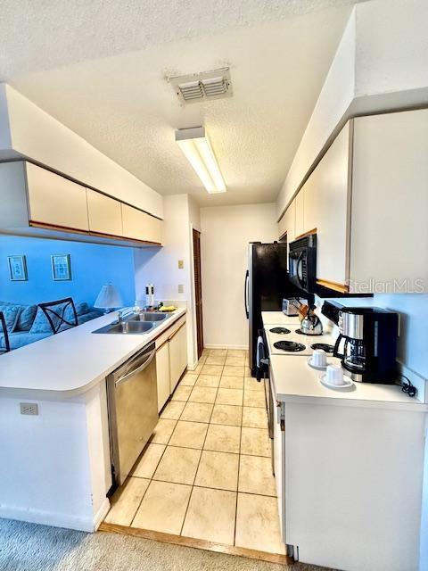 kitchen with sink, white cabinetry, a textured ceiling, light tile patterned floors, and stainless steel dishwasher