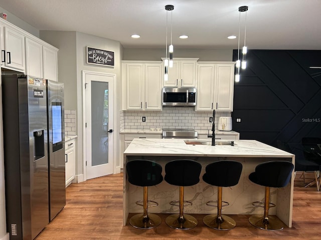 kitchen featuring stainless steel appliances, white cabinets, light stone counters, and decorative light fixtures