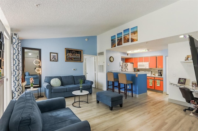 living room with vaulted ceiling, light hardwood / wood-style floors, and a textured ceiling