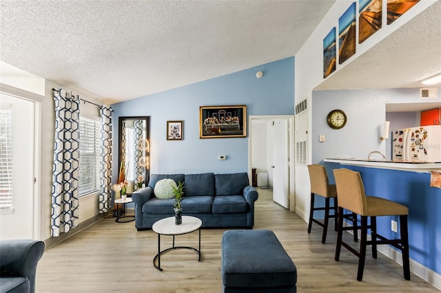 living room featuring vaulted ceiling, a textured ceiling, and light wood-type flooring