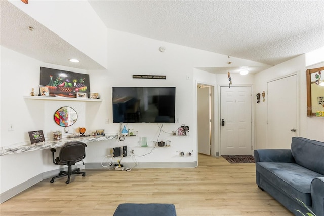 living room featuring vaulted ceiling, built in desk, a textured ceiling, and light wood-type flooring