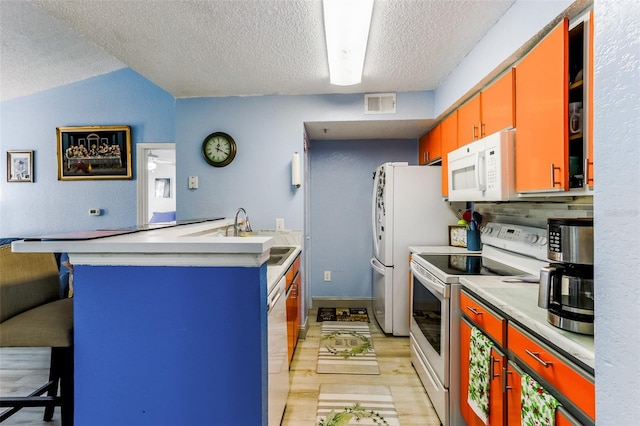 kitchen with sink, white appliances, a breakfast bar, light hardwood / wood-style floors, and a textured ceiling