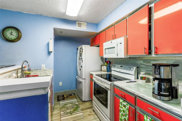 kitchen with sink, white appliances, a textured ceiling, decorative backsplash, and light wood-type flooring