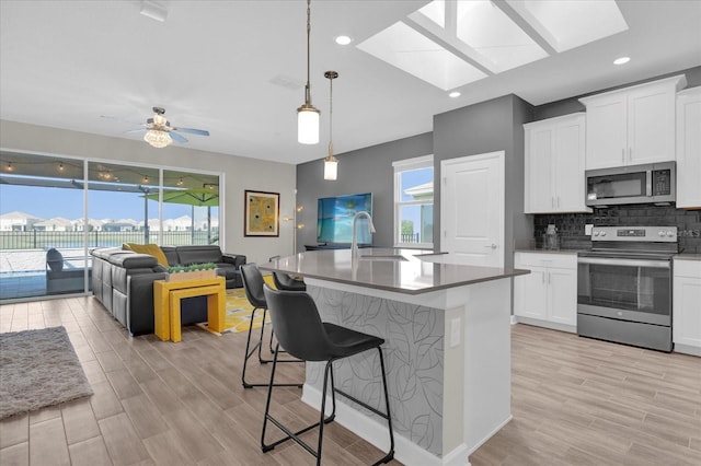 kitchen with sink, appliances with stainless steel finishes, white cabinetry, a kitchen breakfast bar, and a center island with sink