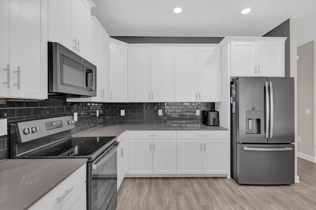 kitchen with appliances with stainless steel finishes, white cabinets, backsplash, and light hardwood / wood-style floors