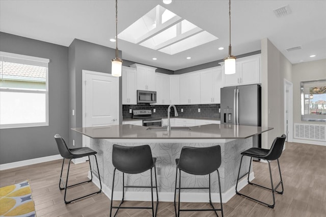 kitchen with stainless steel appliances, an island with sink, pendant lighting, and white cabinets