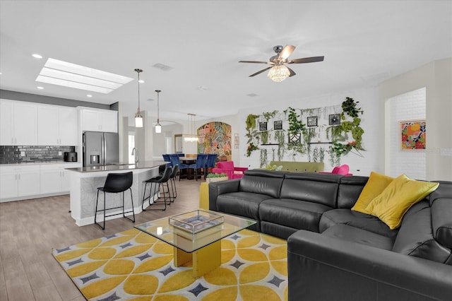 living room with ceiling fan, light hardwood / wood-style floors, and a skylight