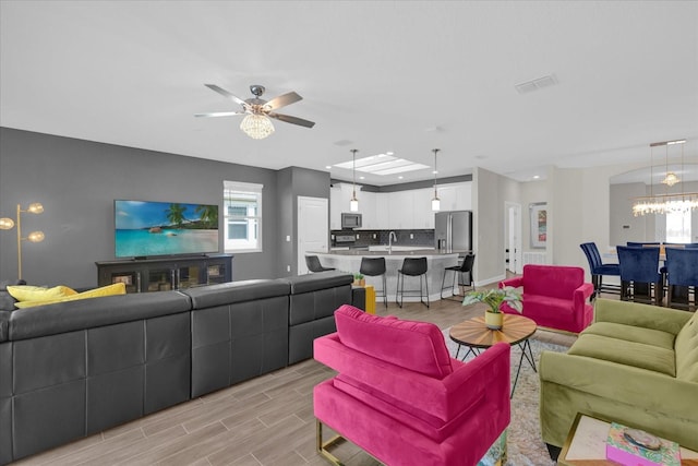 living room featuring ceiling fan with notable chandelier and sink