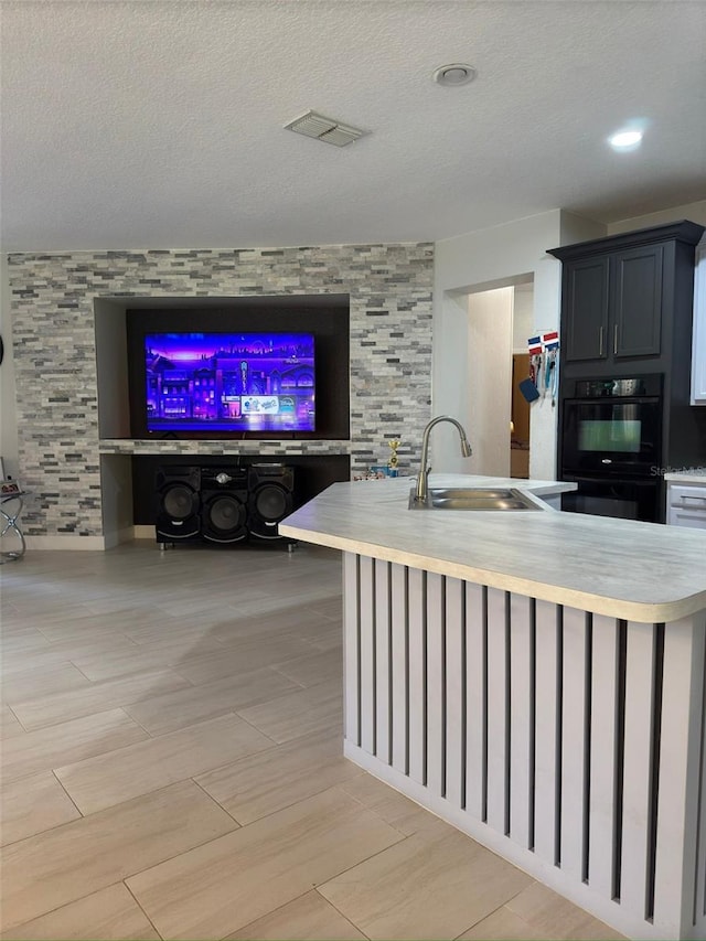 kitchen with black double oven, sink, a kitchen island with sink, and a textured ceiling