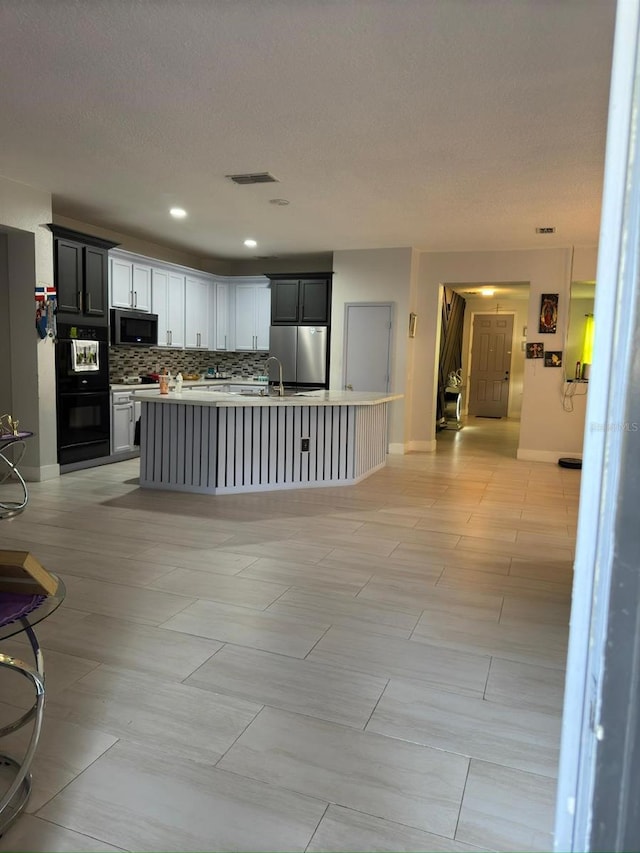 kitchen featuring a kitchen island with sink, white cabinetry, stainless steel appliances, tasteful backsplash, and a textured ceiling