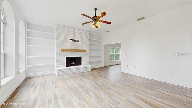 unfurnished living room with ceiling fan, a brick fireplace, light wood-type flooring, and built in shelves