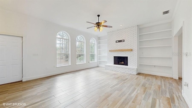 unfurnished living room featuring a brick fireplace, built in shelves, light hardwood / wood-style flooring, and ceiling fan