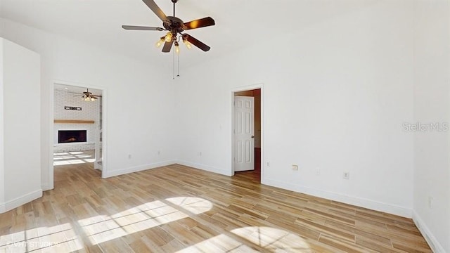 unfurnished room with ceiling fan, a brick fireplace, and light wood-type flooring