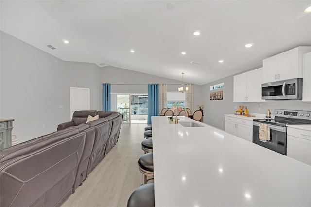 kitchen with sink, appliances with stainless steel finishes, hanging light fixtures, white cabinets, and vaulted ceiling