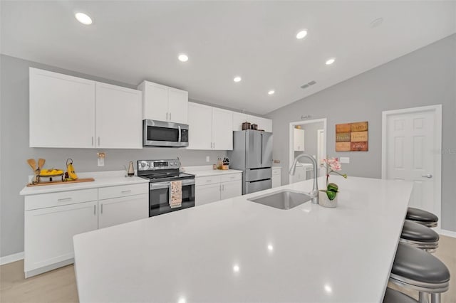 kitchen with appliances with stainless steel finishes, white cabinetry, an island with sink, sink, and a breakfast bar area