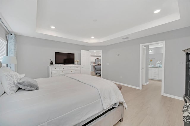 bedroom with ensuite bathroom, a raised ceiling, and light hardwood / wood-style floors