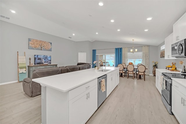 kitchen with lofted ceiling, sink, white cabinetry, appliances with stainless steel finishes, and a kitchen island with sink