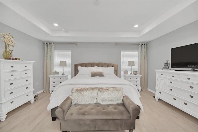 bedroom with a raised ceiling, multiple windows, and light wood-type flooring