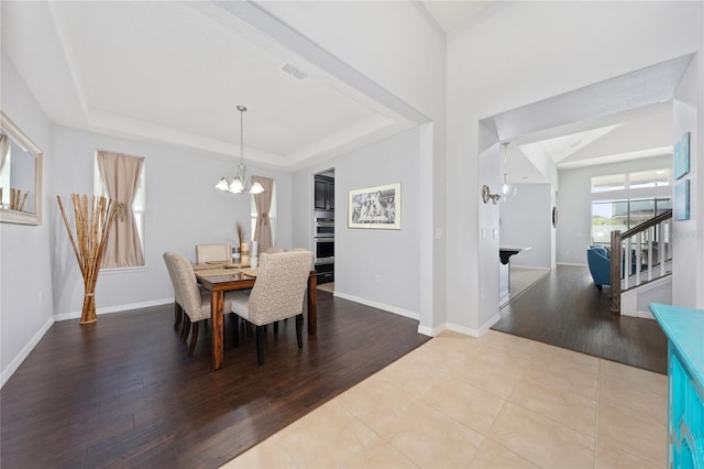 dining room featuring an inviting chandelier, a raised ceiling, and light wood-type flooring