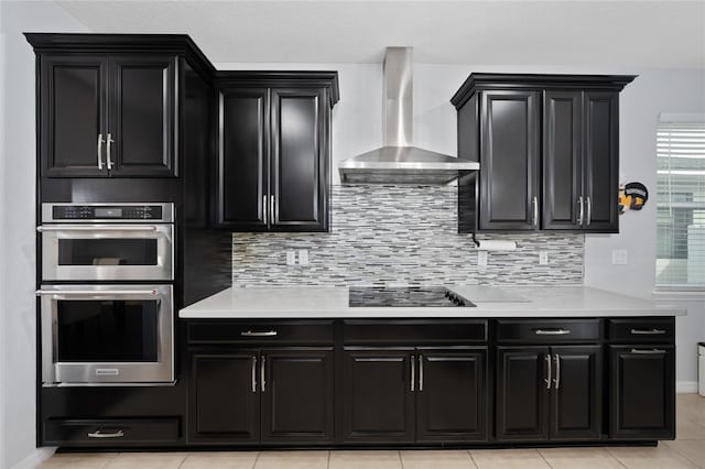 kitchen with double oven, backsplash, light tile patterned floors, black electric stovetop, and wall chimney exhaust hood