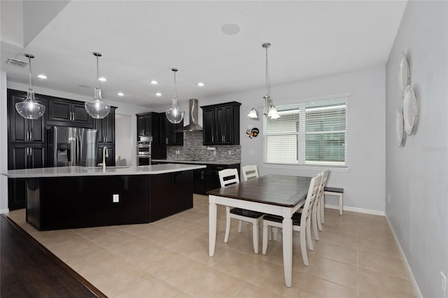 kitchen with decorative light fixtures, a center island with sink, stainless steel appliances, decorative backsplash, and wall chimney range hood