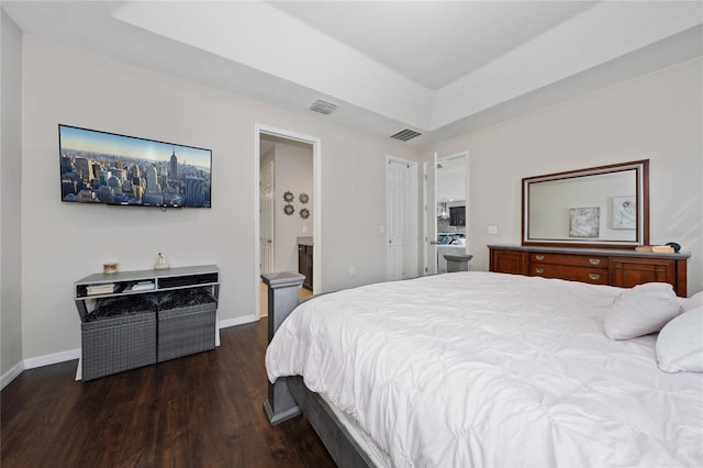 bedroom with ensuite bathroom, dark hardwood / wood-style floors, and a tray ceiling