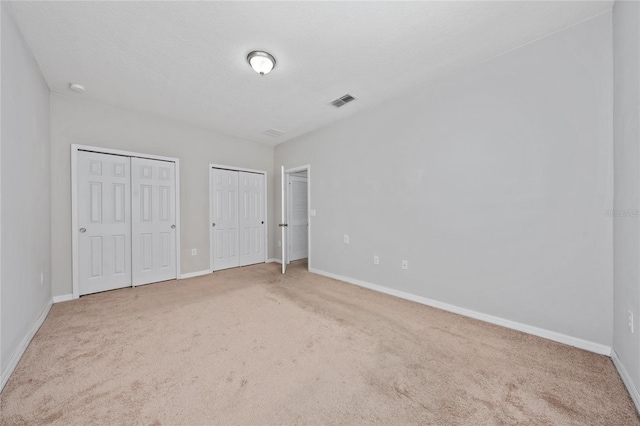 unfurnished bedroom featuring multiple closets, carpet, and a textured ceiling