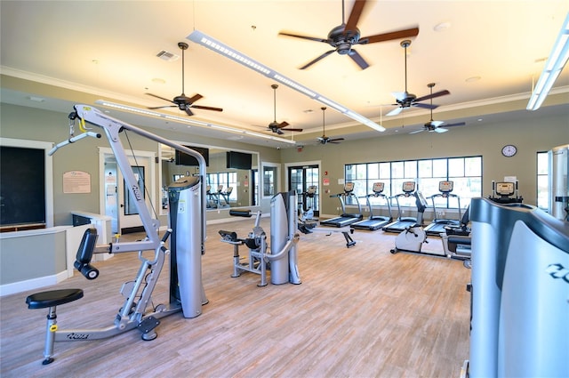 workout area featuring a raised ceiling, crown molding, and light wood-type flooring