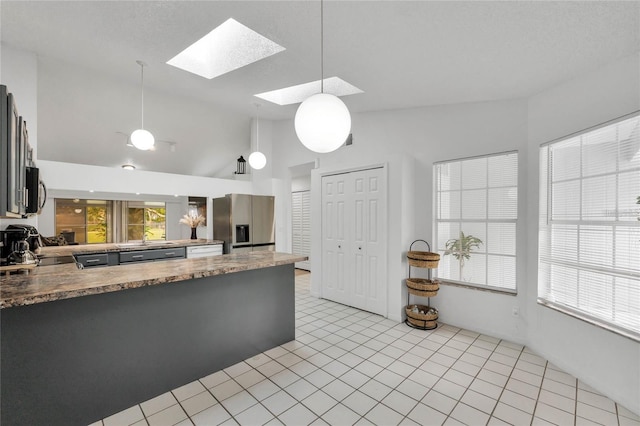 kitchen with light tile patterned floors, stainless steel fridge, vaulted ceiling with skylight, decorative light fixtures, and kitchen peninsula