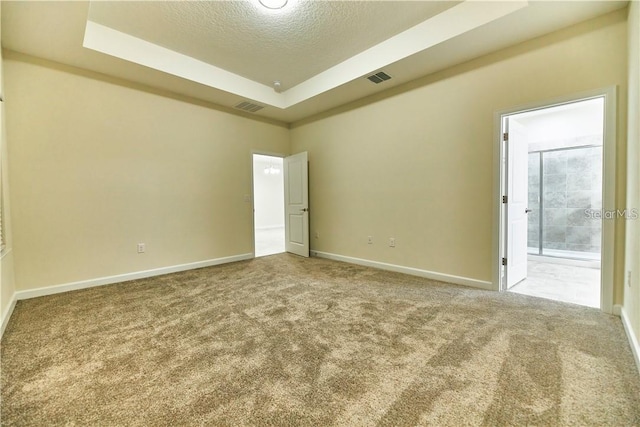 unfurnished bedroom with a tray ceiling, carpet floors, ensuite bath, and a textured ceiling