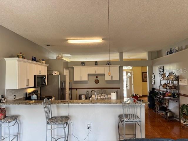 kitchen with white cabinetry, black refrigerator, a kitchen breakfast bar, and kitchen peninsula