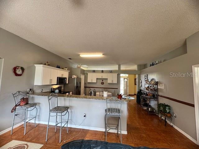 kitchen featuring a breakfast bar area, stainless steel fridge with ice dispenser, a textured ceiling, kitchen peninsula, and white cabinets