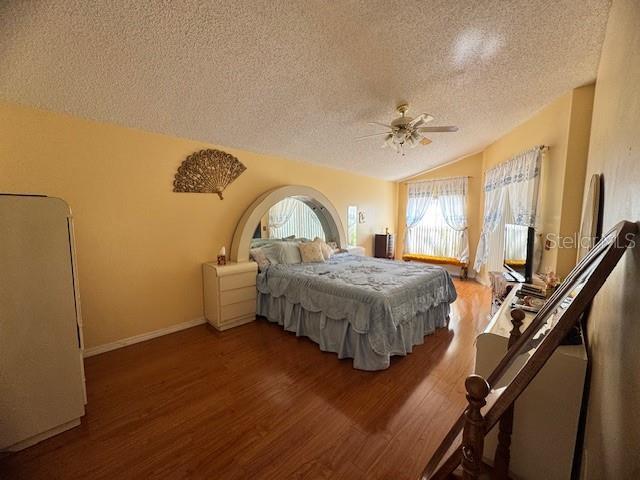 bedroom with lofted ceiling, dark wood-type flooring, ceiling fan, refrigerator, and a textured ceiling