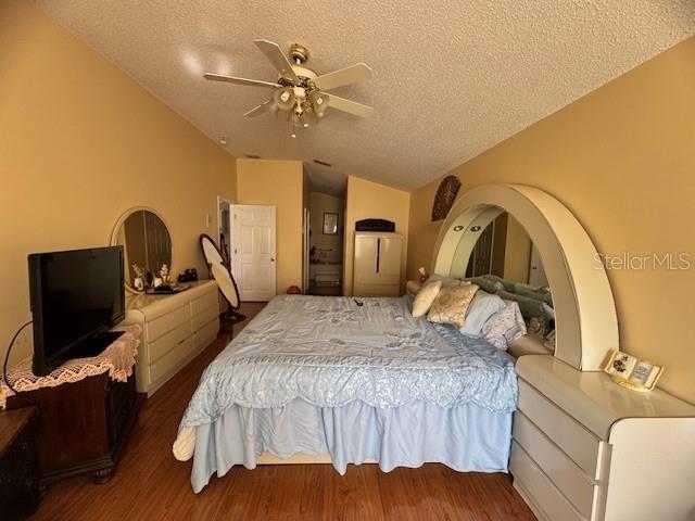 bedroom featuring dark hardwood / wood-style flooring, ceiling fan, vaulted ceiling, and a textured ceiling