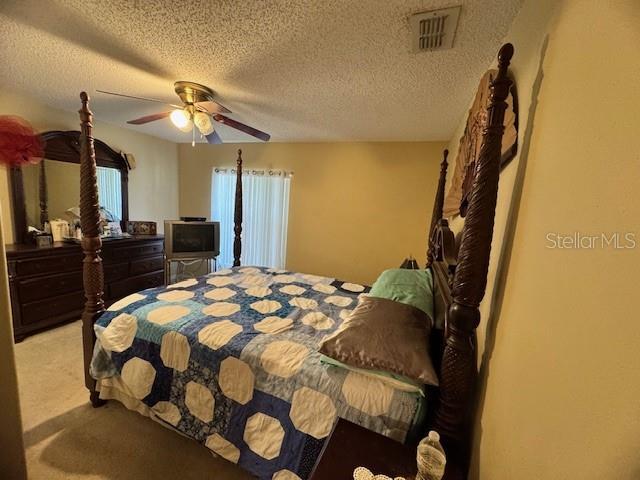 bedroom featuring light carpet, a textured ceiling, and ceiling fan