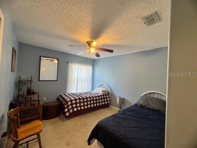 bedroom with ceiling fan, carpet floors, and a textured ceiling