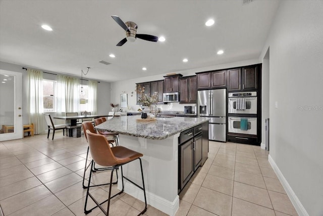 kitchen with light tile patterned flooring, appliances with stainless steel finishes, a center island, and light stone counters