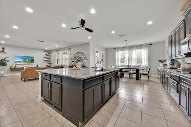 kitchen with light tile patterned flooring, a kitchen island with sink, light stone counters, and pendant lighting