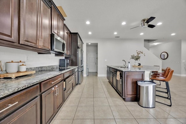 kitchen with sink, a breakfast bar area, a center island with sink, appliances with stainless steel finishes, and light stone countertops