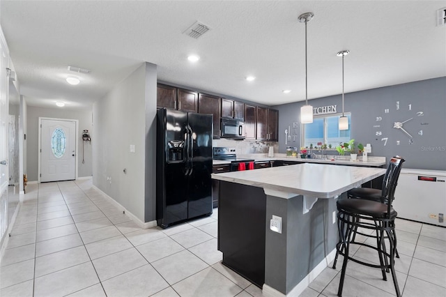 kitchen featuring light tile patterned flooring, a breakfast bar, a center island, black appliances, and dark brown cabinets