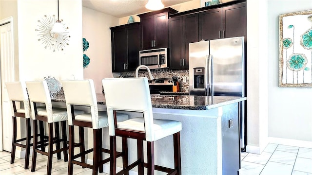 kitchen with tasteful backsplash, hanging light fixtures, dark stone counters, a kitchen breakfast bar, and stainless steel appliances