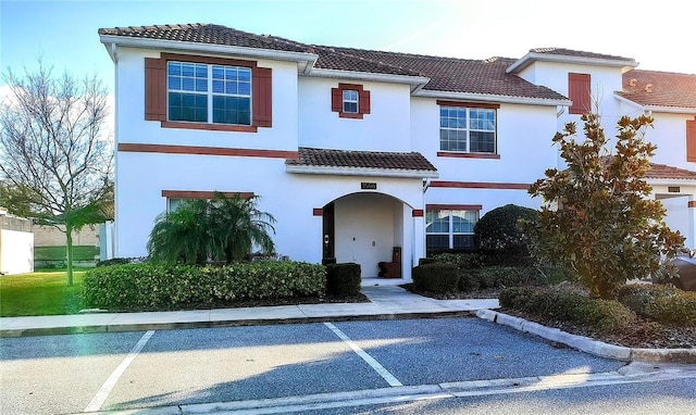 mediterranean / spanish home featuring stucco siding, a tiled roof, and uncovered parking