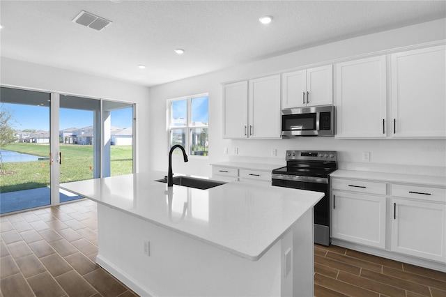 kitchen featuring visible vents, appliances with stainless steel finishes, a kitchen island with sink, light countertops, and a sink