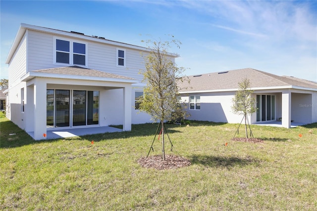 back of house featuring a shingled roof, a lawn, and stucco siding