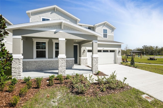 view of front of property featuring a garage, driveway, stone siding, covered porch, and a front lawn