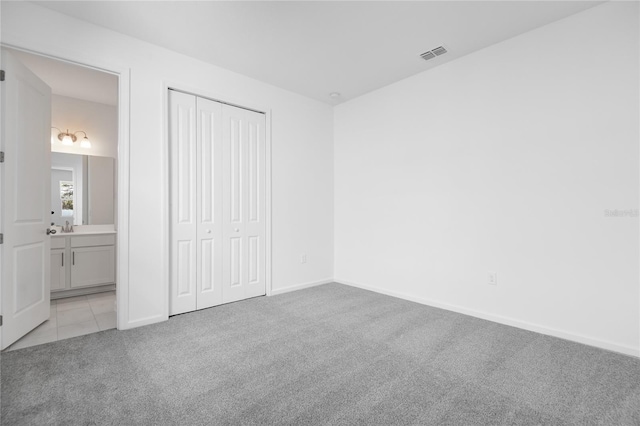 unfurnished bedroom featuring baseboards, visible vents, connected bathroom, light colored carpet, and a closet