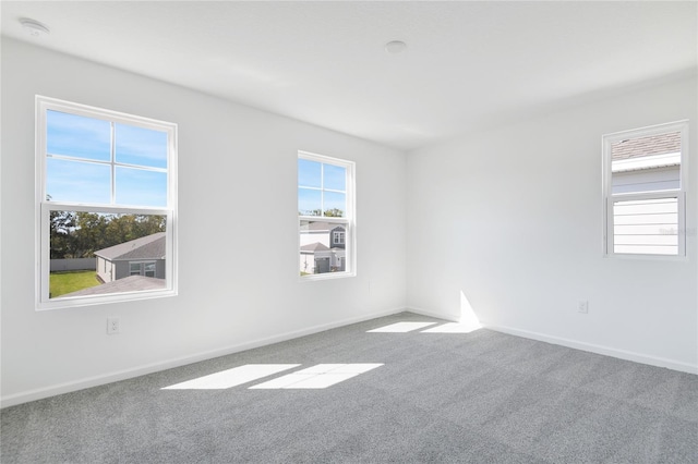 spare room featuring carpet floors, plenty of natural light, and baseboards